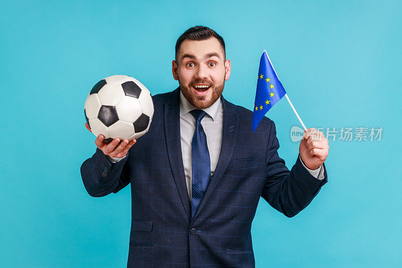 兴奋的男子穿着官方风格的西装，手持黑白足球和欧盟旗帜，观看足球和支持喜爱的球队。
