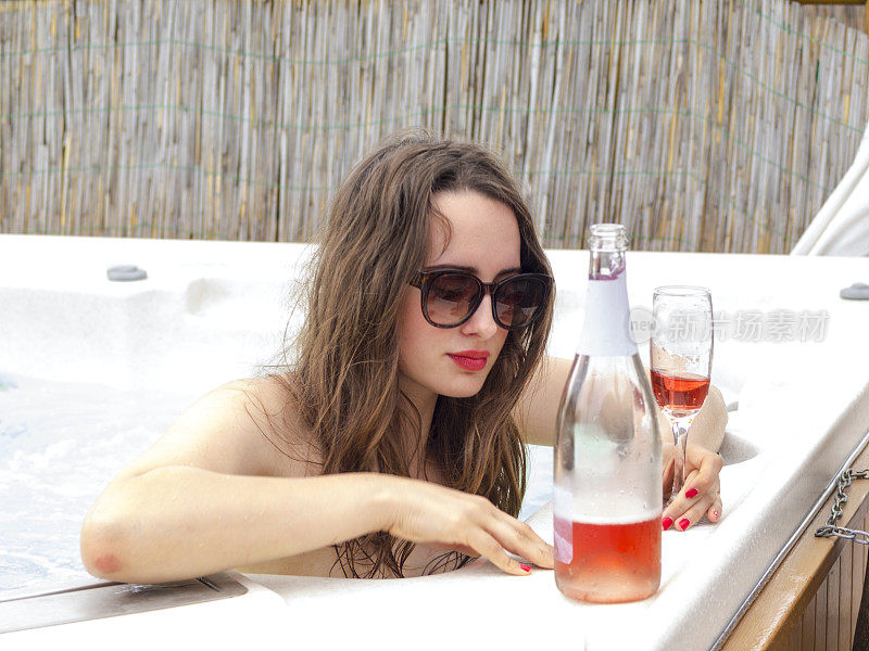 年轻的女士戴着墨镜，喝着甜葡萄酒在热水浴缸里