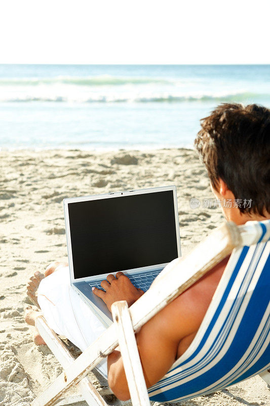 一个年轻人一边用笔记本电脑工作，一边在海滩上休息