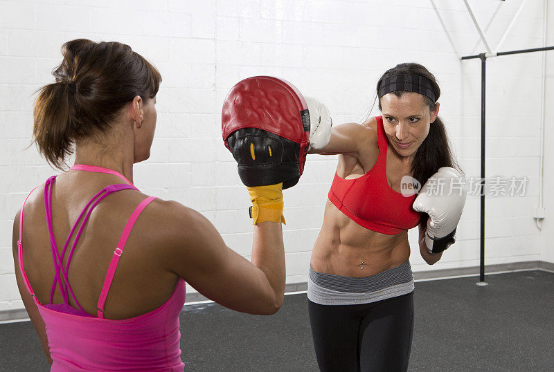 女运动员与教练进行拳击训练。