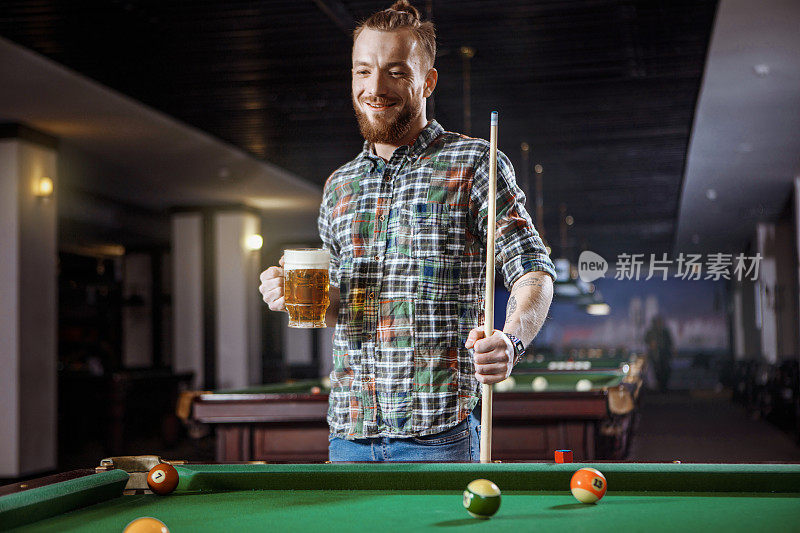 一个年轻人站在台球俱乐部里，手里拿着啤酒
