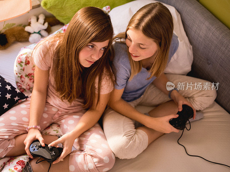 女孩们穿着睡衣在床上玩电脑游戏