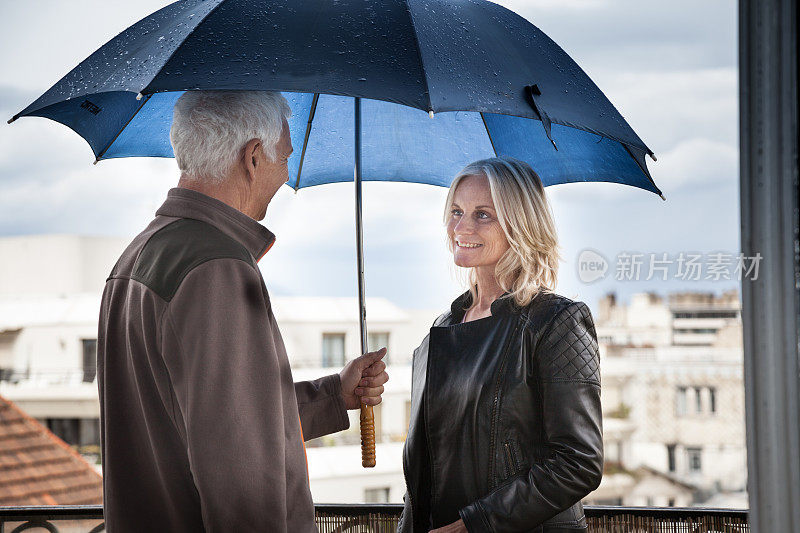 一对成熟的夫妇在巴黎的公寓阳台上冒雨