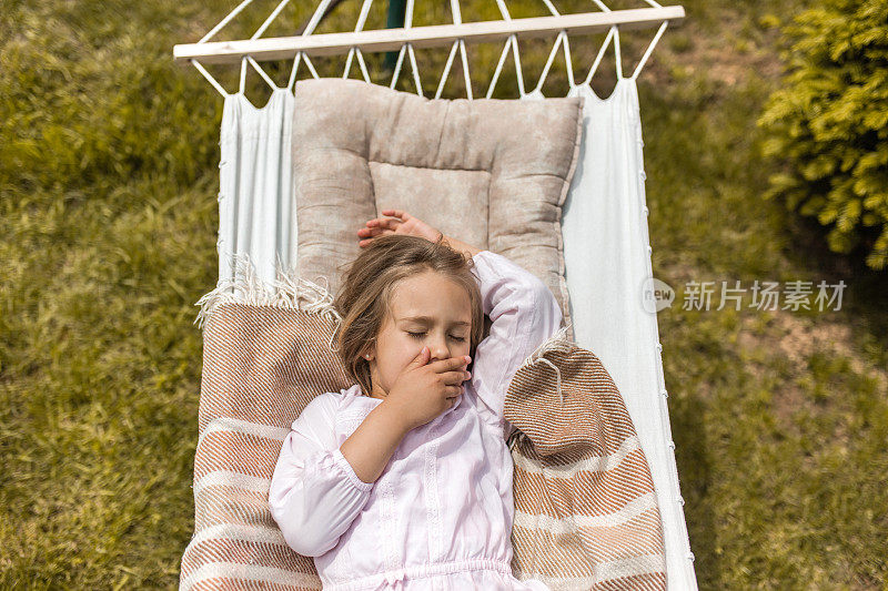 上图是疲惫的小女孩在吊床上打哈欠。