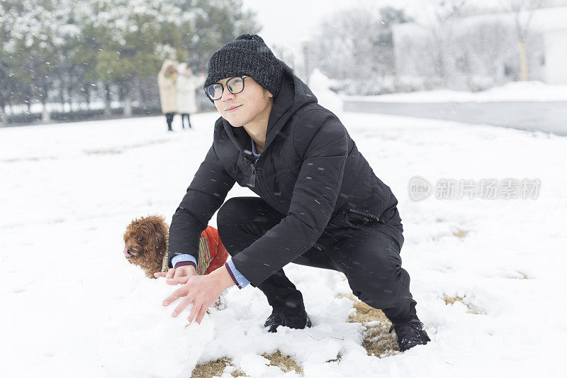 男人和宠物狗在雪地上滚雪球