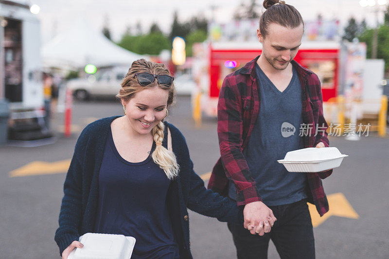 一对年轻的夫妇走过一个食品推车，里面装着他们的外带午餐盒