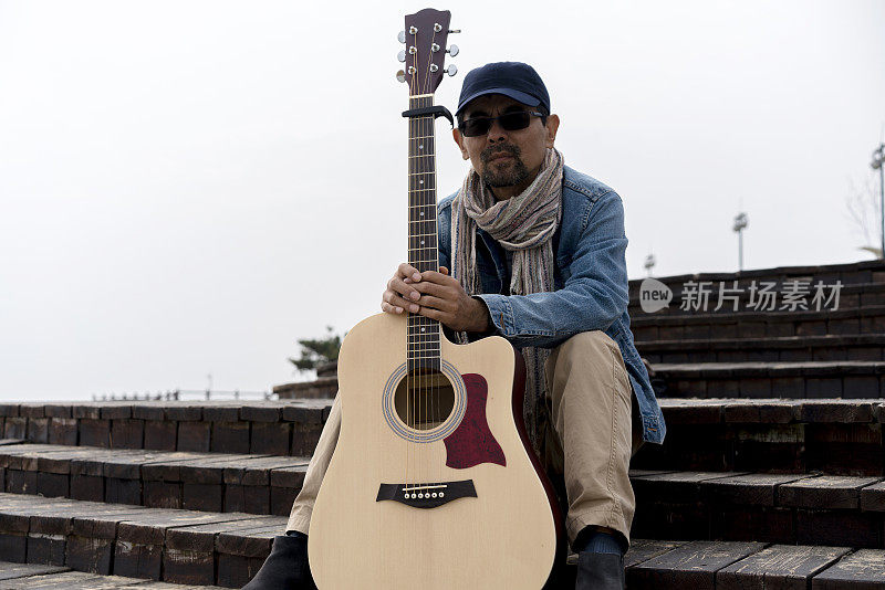 一个拿着吉他的男人坐在海边的木板路上