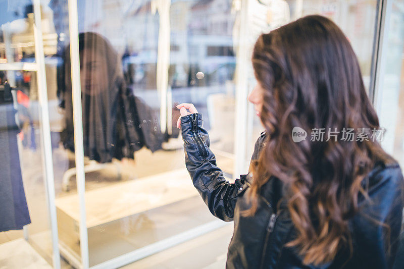 美丽时尚的女孩走在城市里，看着商店的橱窗。