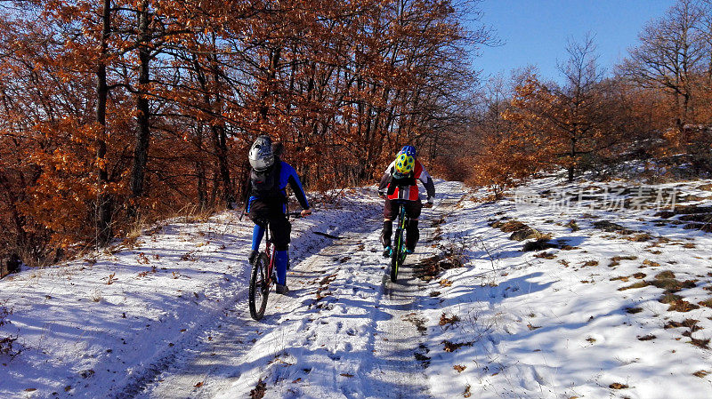 在美丽的冬日里，两名山地自行车手在一条覆盖着积雪的土路上骑行