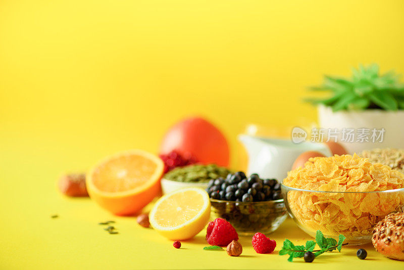 谷类玉米，什锦麦片，牛奶，浆果，橙汁，酸奶，煮鸡蛋，坚果，水果，香蕉，桃子早餐在黄色的背景。副本的空间。纯素和素食的概念。