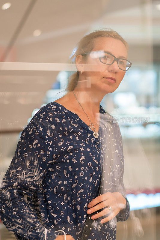 从商店橱窗里看购物的中年妇女