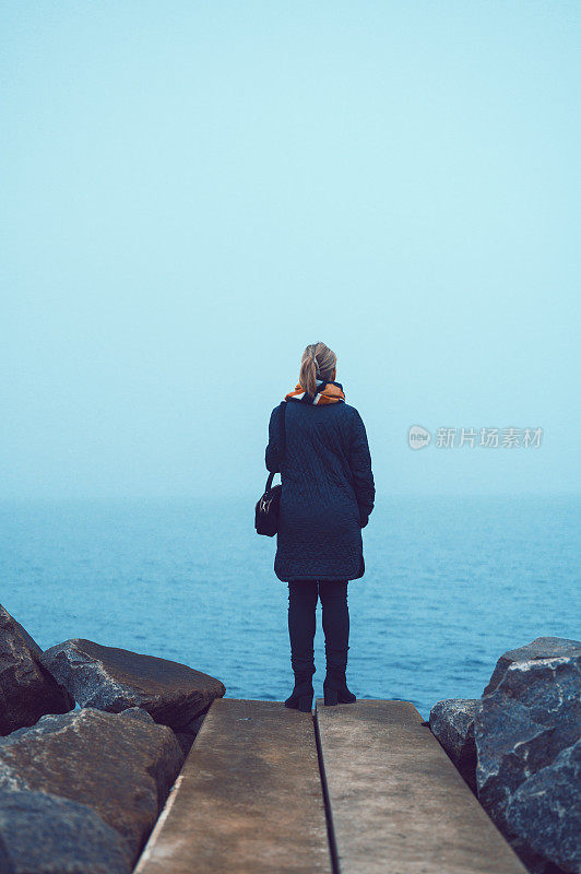 后视图的女人站在海边在一个寒冷和阴天
