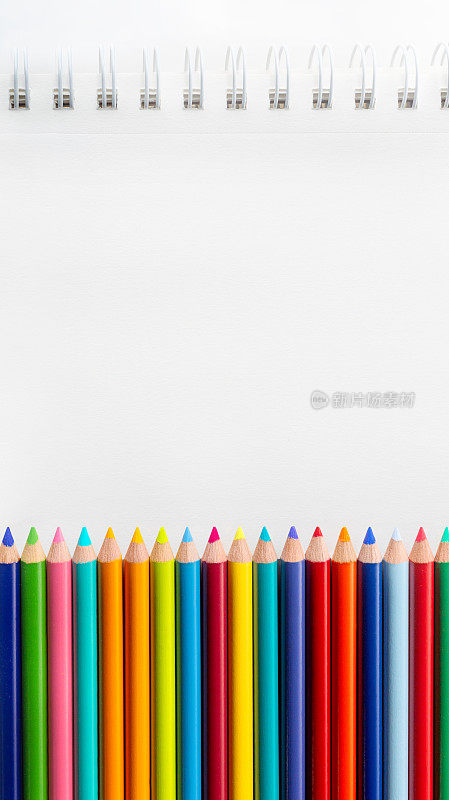 一排彩色铅笔在空白的白色素描簿纸上。在干净的白纸上复制空白。背景照片，用于艺术课或学校的信息、海报或签名。