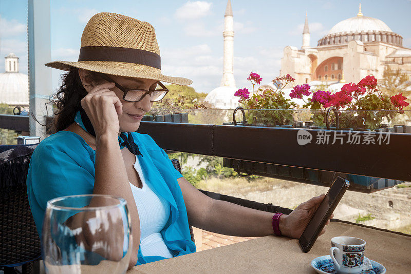 一名女游客坐在伊斯坦布尔的一个露台咖啡馆里，正在搅动她的手机。