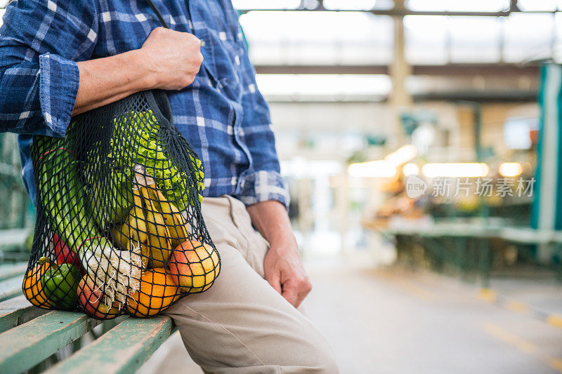 成年人与水果和蔬菜在一个黑色棉网可重复使用的袋子，零浪费购物在户外市场