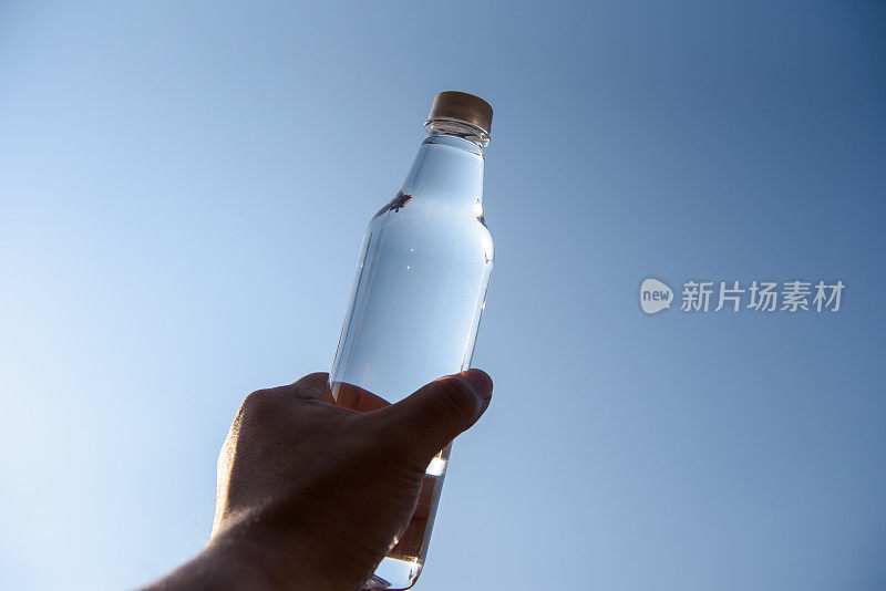 在蓝天里，男人手里拿着晶莹剔透的水瓶
