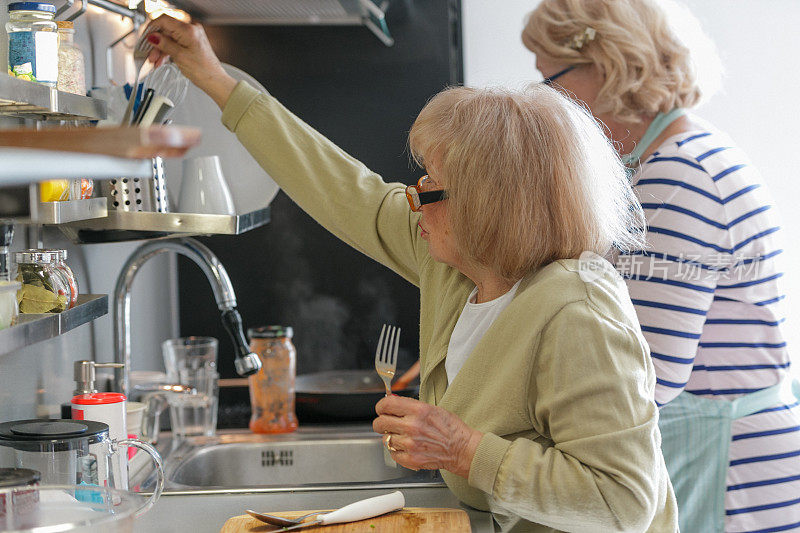 成熟的女人由她的朋友在厨房里伸手拿叉子