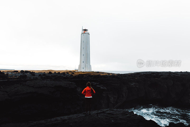 一名身穿红色夹克的女子正在欣赏冰岛美丽的灯塔和悬崖
