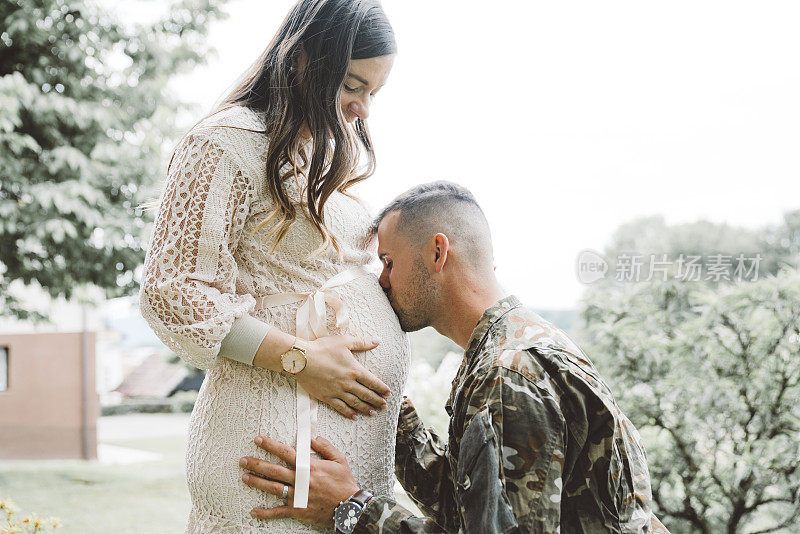 穿着军装的男人亲吻他怀孕的妻子的肚子