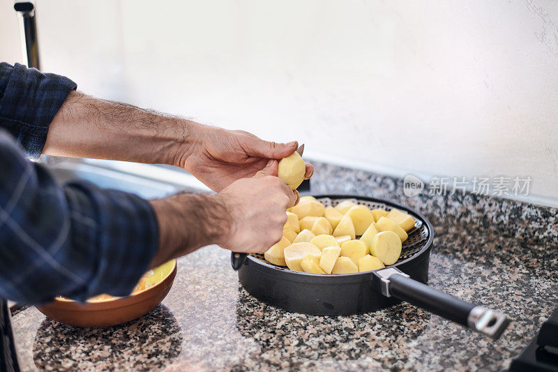 检疫烹饪:一名男子正在削土豆皮，并把它们放在锅里