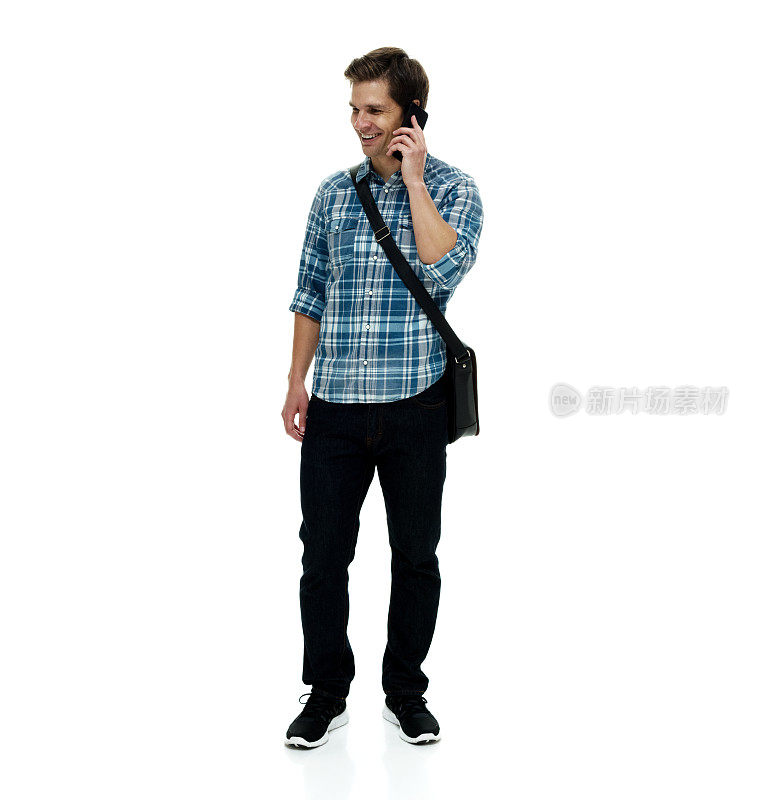 白人青年男性站在白色背景前，带着邮差包，拿着包，使用手机