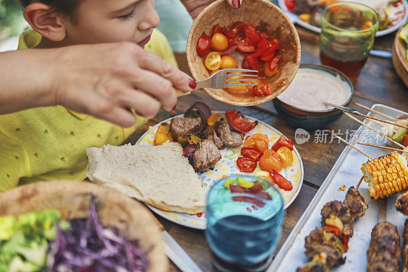 年轻的家庭在外面吃羊肉，牛肉和蔬菜串和绿色沙拉