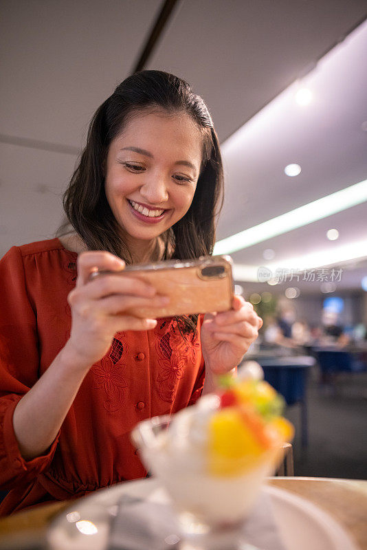 快乐的年轻女子在红色连衣裙拍照的甜点在咖啡馆