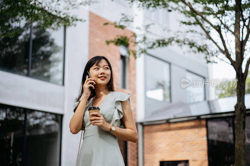 年轻时尚的亚洲女人拿着外卖咖啡和打电话