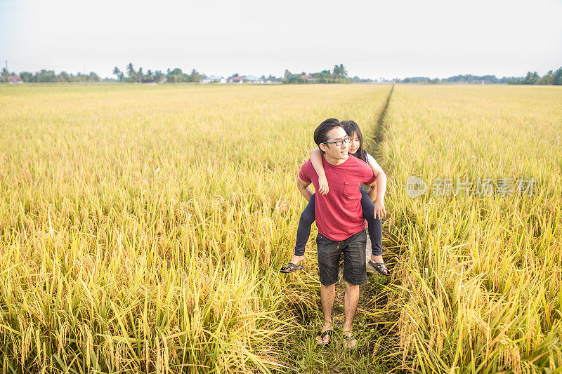一个成熟的中国父亲背着女儿在稻田里