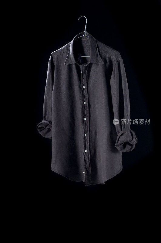 衣服:挂在衣架上的棕色衬衫，背景是黑色。