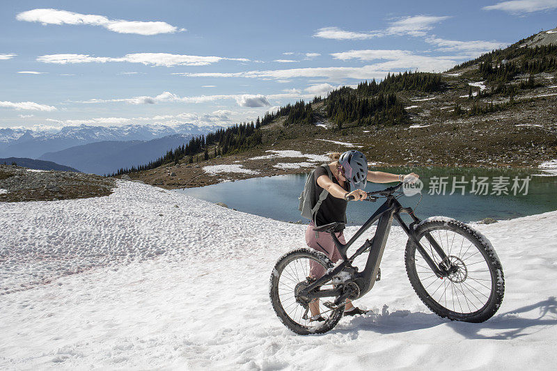 年轻女子推着山地电动自行车爬上雪坡