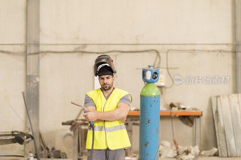 建筑工人在一个加压气瓶旁摆姿势，双臂交叉看着摄像机