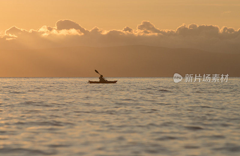 女子划着海上皮艇在夕阳与金色的光辉