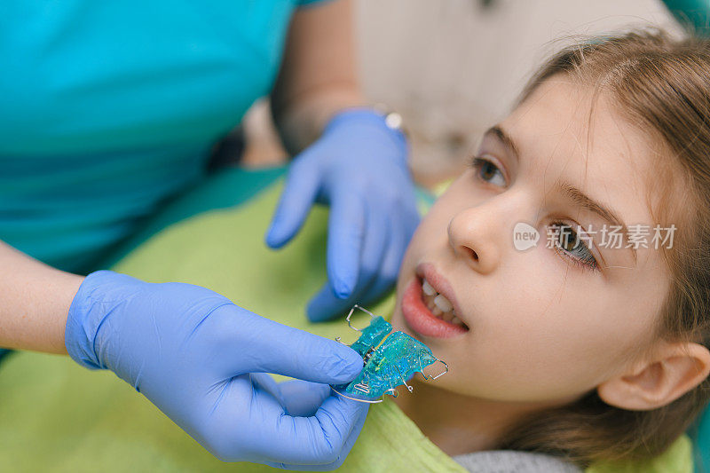当牙医在给她装牙箍时，女孩坐在牙科椅上。