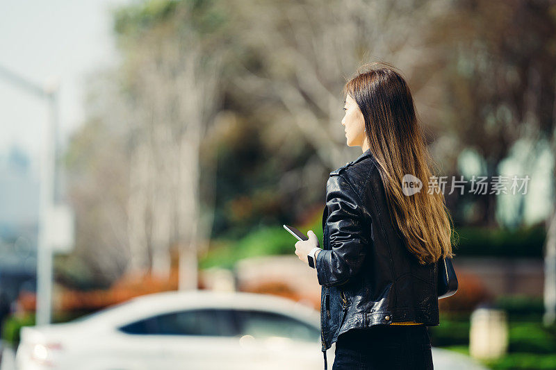 自信的亚洲女商人在城市里拿着智能手机。