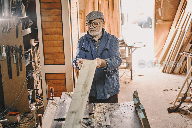 一个老木匠，他正在一个旧车间里做一块木板。