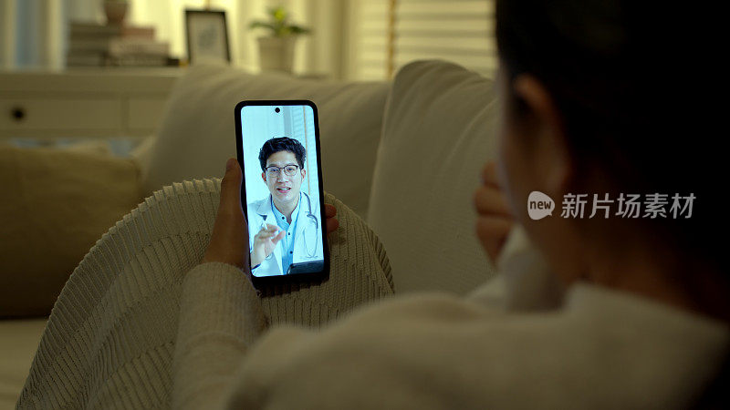 在肩膀上看年轻的亚洲妇女与医生在手机视频会议医疗应用程序在远程医疗在线服务医院隔离社会距离深夜的概念。