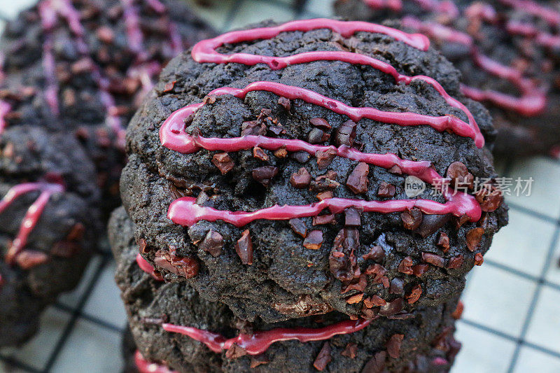 特写图片是一堆新鲜烘焙的，自制的，巧克力片黑森林饼干，装饰着粉红色的水糖霜，在电线上，金属冷却架上面的防油纸羊皮纸，聚焦前景
