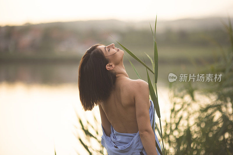 年轻的性感女人赤裸的肩膀站在自然和手持植物