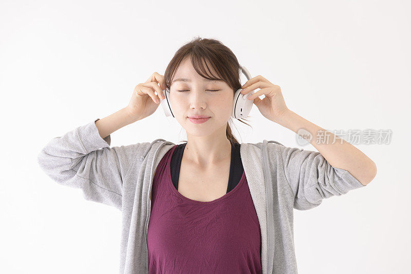 一名年轻女子戴着耳机，闭着眼睛在白色背景前听音乐。