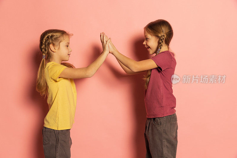 活泼的小女孩，姐妹或兄弟姐妹穿着休闲风格的衣服，在粉红色的背景下独自玩耍。童年的概念，情感