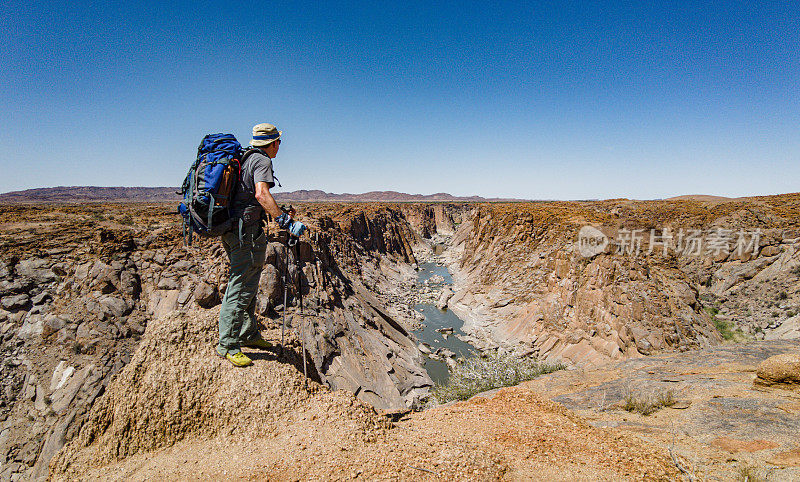 一个背着背包的徒步旅行者在一个干旱的沙漠地区徒步旅行，看风景下的峡谷