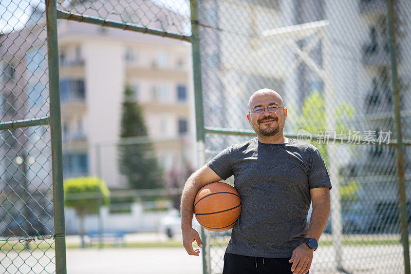 一个戴眼镜的又矮又胖的年轻人在附近的篮球场上打街头篮球
