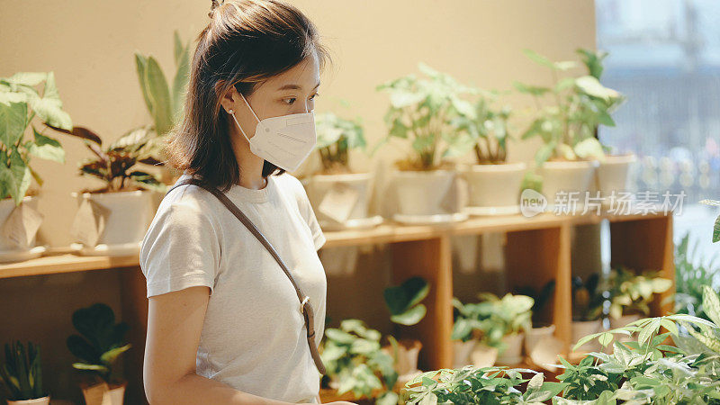 年轻的亚洲女性顾客戴着防护口罩在花园中心购买植物