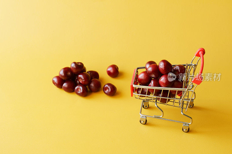 超市里的金属手推车里装着新鲜的红樱桃。在商店里买浆果和水果的概念。黄色背景。