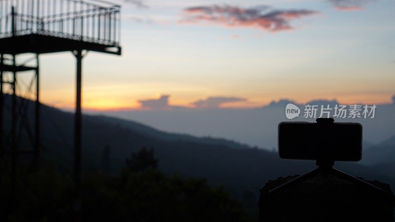 三脚架上的智能手机捕捉山景日出的延时。移动摄影或摄像概念
