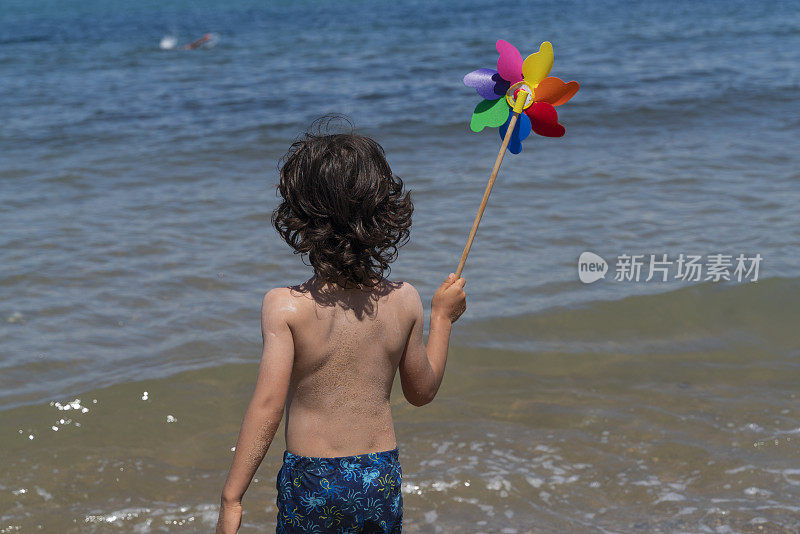 从后面可以看到一个走向大海的男孩。拿着五彩缤纷的风向标