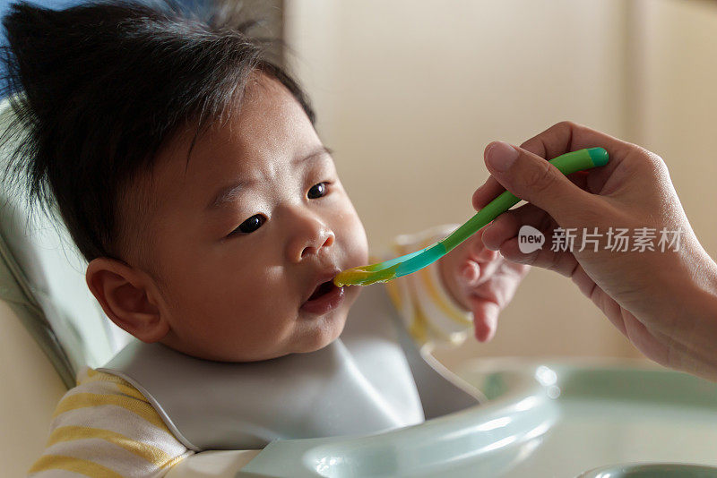 坐在高椅子上的亚洲小男孩正在被妈妈喂食。