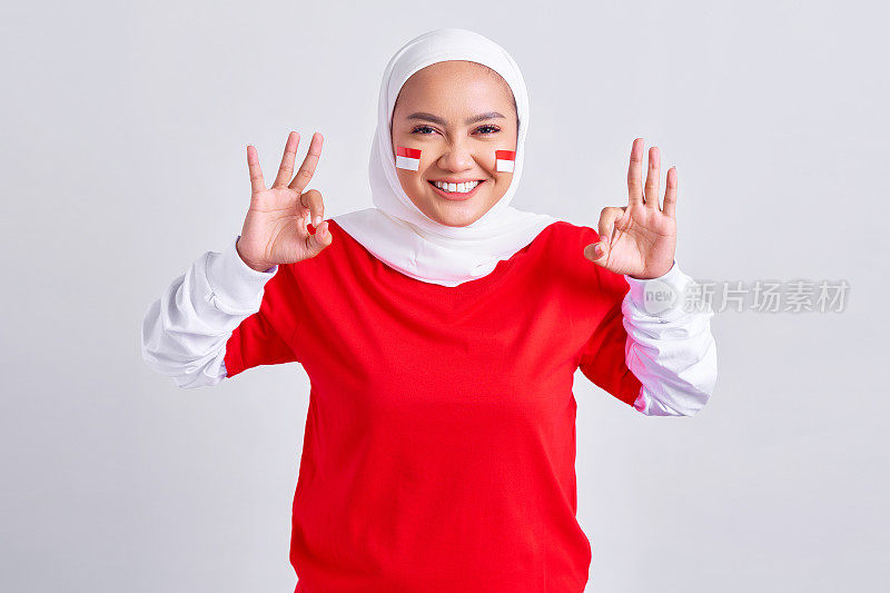 激动的年轻亚洲穆斯林妇女穿着红白t恤庆祝8月17日印度尼西亚独立日，并在白色背景上显示出okay的手势