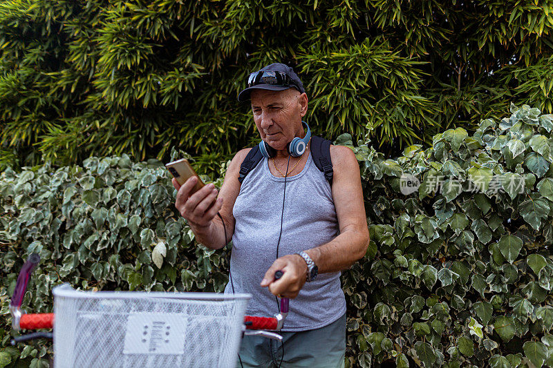 一位骑自行车的老人站在人行道上看手机